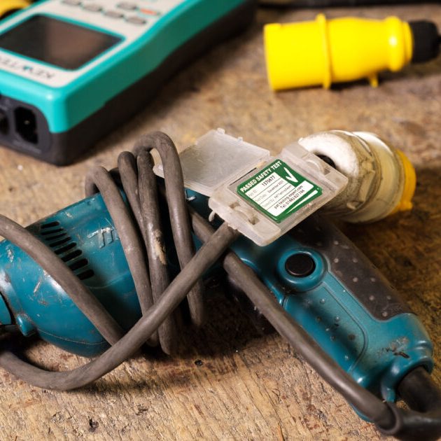 Construction Site Safety Testing A blue power tool with a coiled cord and a yellow 110V plug on a wooden surface.