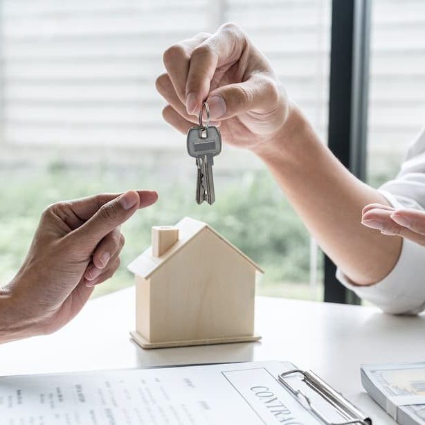 Landlords and Estate Agents A person handing over house keys with a model house on a table.